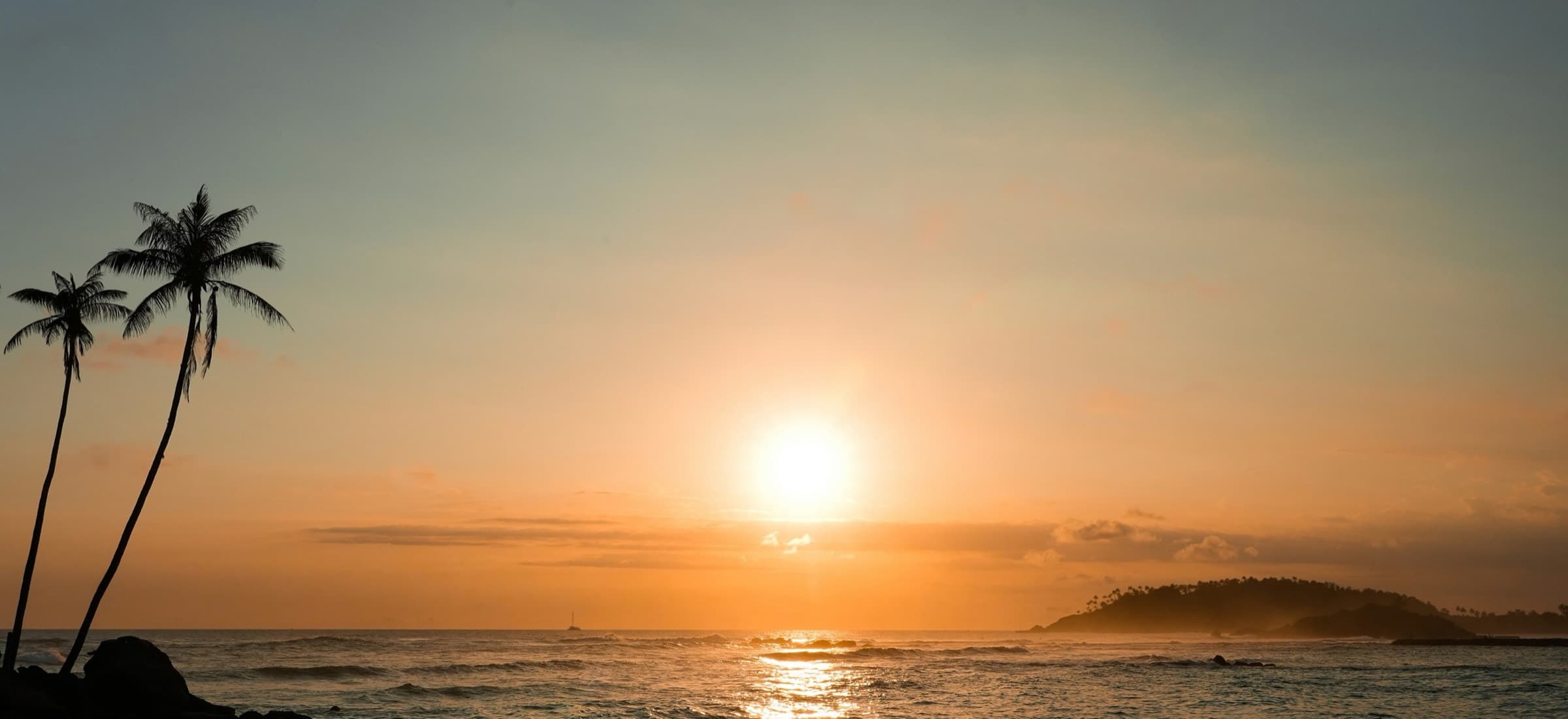 Sunset over a rocky Sri Lankan beach with leaning coconut palms